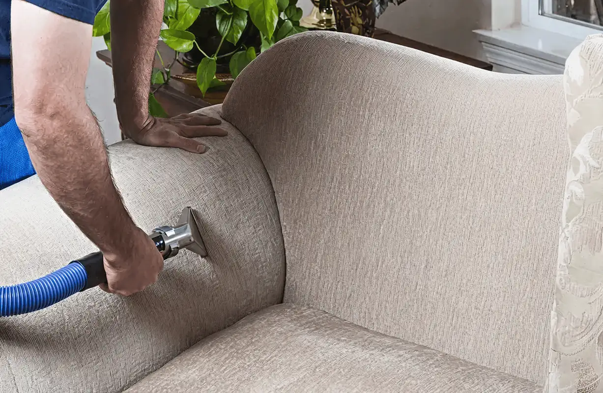 Professional upholstery cleaner deep-cleaning a fabric sofa with a handheld extraction tool and hose, Orange, CA.
